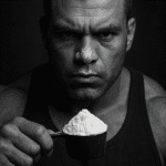 A bodybuilder holding a scoop of protein powder in front of his face.
